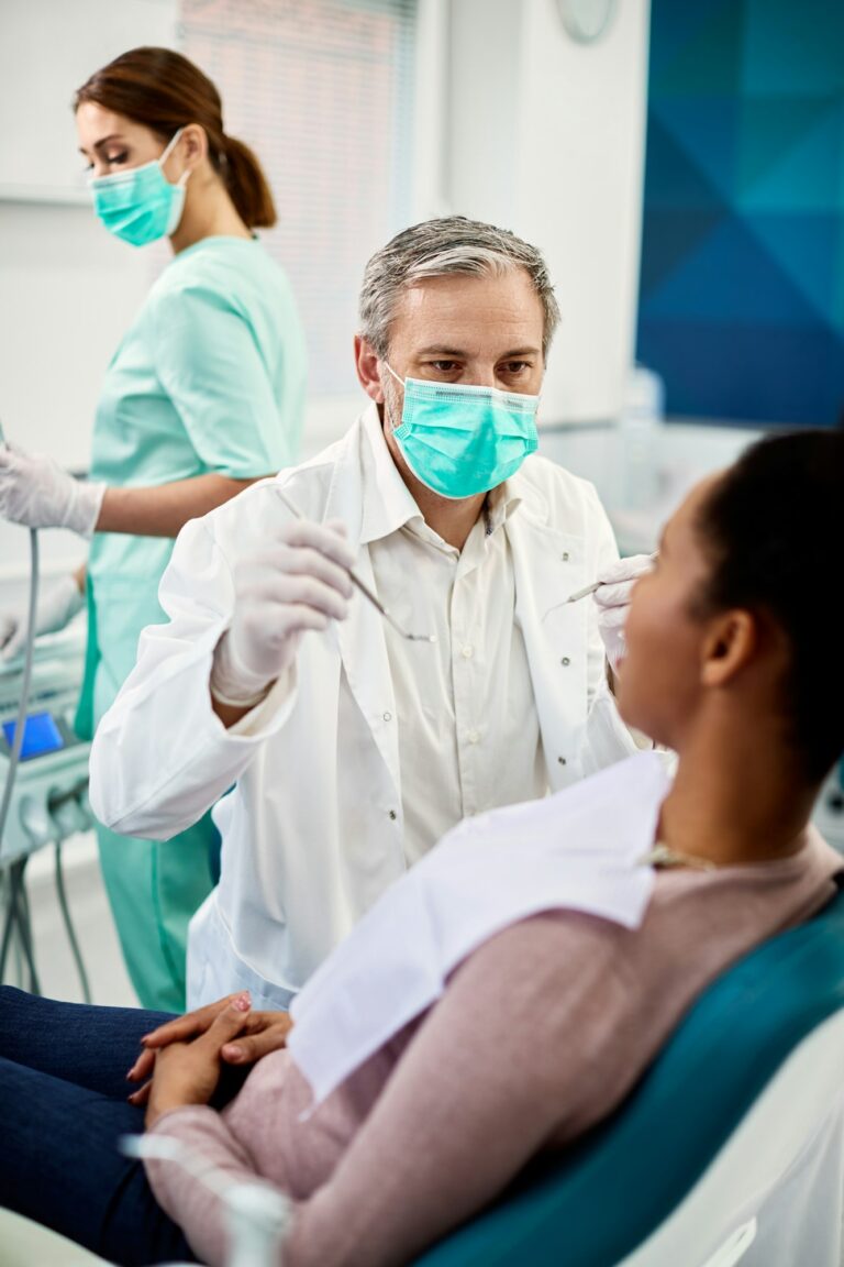 Male dentist examining teeth of black woman during appointment at dentist's office.